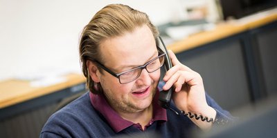 Ein Mann mit Brille spricht lächelnd am Telefon, während er in einem modernen Büro sitzt.