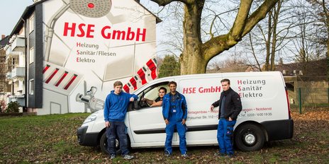 Die Mitarbeiter der HSE GmbH posieren vor ihrem Fahrzeug, das mit Informationen über Heizungs- und Sanitärdienstleistungen beschriftet ist.