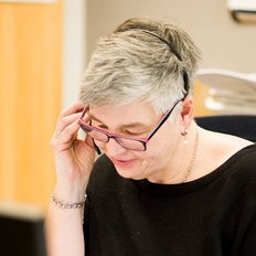 Eine Frau mit grauen Haaren trägt ein Headset und spricht am Telefon, während sie auf ihren Computerbildschirm schaut.
