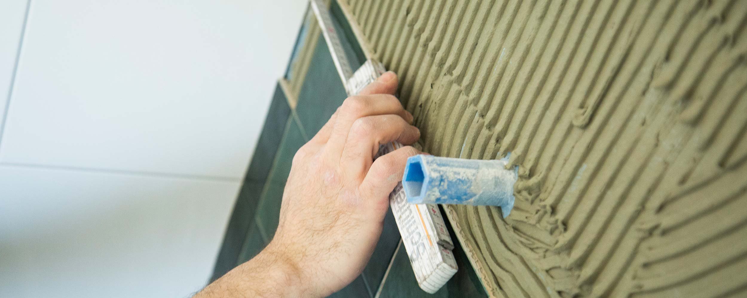 Eine Hand trägt Mörtel auf eine Wand auf, während eine Kelle mit blauer Spitze verwendet wird, um eine gleichmäßige Schicht zu schaffen.