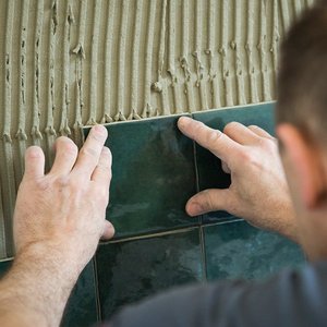 Ein Handwerker platziert sorgfältig eine grüne Fliese an einer Wand mit strukturiertem Mörtel, um ein schönes Muster zu schaffen.
