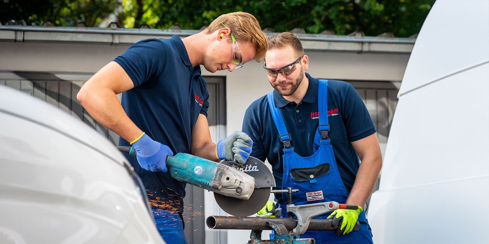 Zwei Handwerker arbeiten konzentriert an einem Metallrohr, während Funken sprühen und sie Schutzausrüstung tragen.