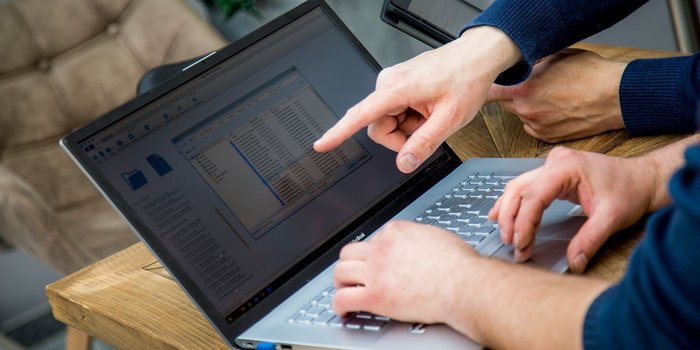 Zwei Hände zeigen auf einen Laptop-Bildschirm, der eine Liste von Dateien in einem Ordner anzeigt, während sie zusammenarbeiten.