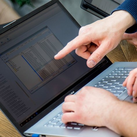 Zwei Hände zeigen auf einen Laptop-Bildschirm, der eine Liste von Dateien in einem Ordner anzeigt, während sie zusammenarbeiten.