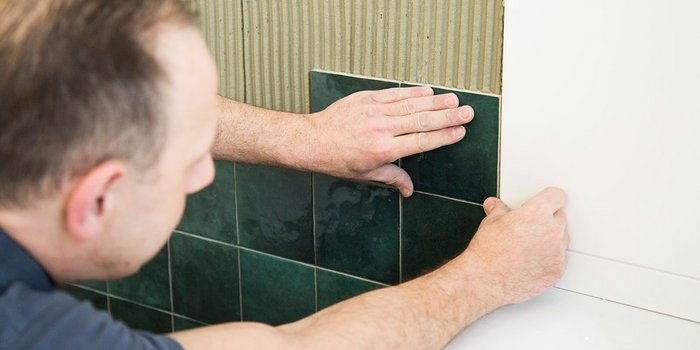 Ein Handwerker verlegt sorgfältig grüne Fliesen an einer Wand, während er die Kanten genau ausrichtet.